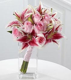 a bouquet of pink roses and lilies in a clear vase on a white table