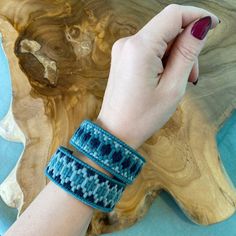 a woman's hand holding onto two bracelets on top of a wooden table