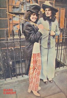 two women standing next to each other in front of a gate with an umbrella on it