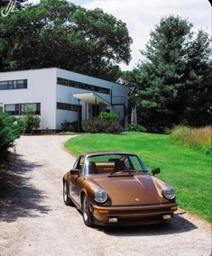 a brown porsche parked in front of a large white building with trees and grass around it