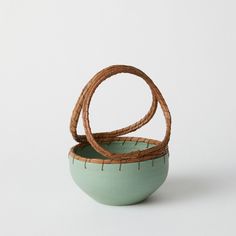 two green bowls sitting next to each other on top of a white surface with brown handles