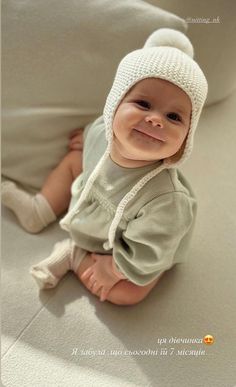 a smiling baby wearing a white knitted hat