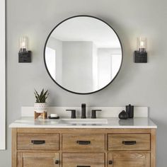 a bathroom vanity with a round mirror above it and two lights on the wall next to it