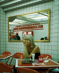 a woman sitting at a table talking on her cell phone in front of a mirror