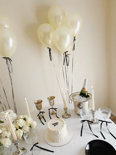 a table topped with lots of white balloons next to a cake and wine glass on top of it