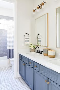 a bathroom with blue cabinets and white counter tops, two mirrors on the wall above the sinks