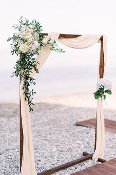 a wedding arch decorated with greenery and white flowers on the beach at night time