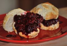 two pastries on a red plate with blueberry sauce in between the buns