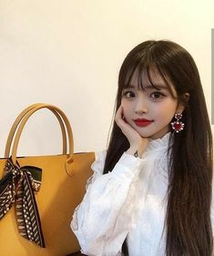 a young woman sitting next to a yellow purse and wearing red lipstick with her hand on her chin