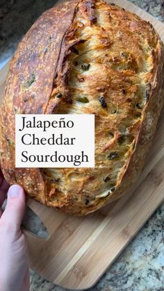 a person holding a piece of bread on top of a cutting board with the words jalapeno cheddar sourdough