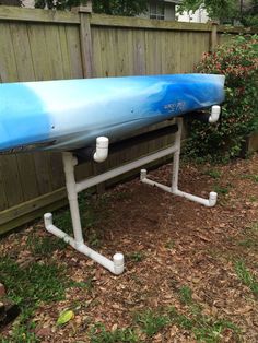 a blue and white surfboard sitting on top of a metal stand next to a fence