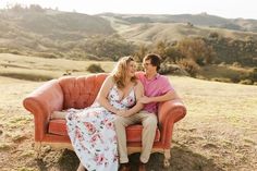 a man and woman are sitting on an orange couch in the middle of a field