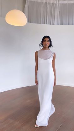 a woman in a white dress standing on a wooden floor next to a light fixture