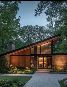 a modern house in the woods with large windows and brick walkway leading up to it