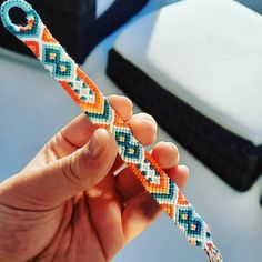 a hand holding an orange, blue and white bracelet on a table next to a laptop