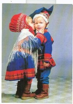 two small children dressed in colorful clothing and boots, one holding the other's head