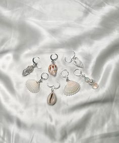 seven seashells are arranged on a white satin sheet with silver earring hooks