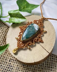 a piece of jewelry sitting on top of a wooden table next to a leafy green plant