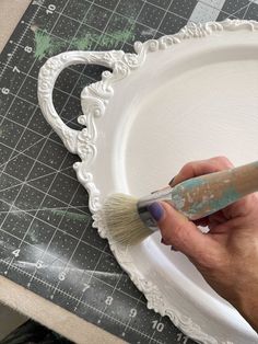 a person using a brush to paint a white plate