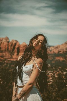 a woman with long hair and tattoos standing in front of the desert, looking off into the distance