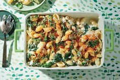 a casserole dish filled with pasta and spinach on a table next to a bowl of broccoli