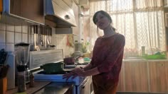 a woman standing in a kitchen next to a stove top oven and counter with pots on it