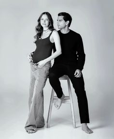 a man and woman sitting on a stool posing for a black and white photo together