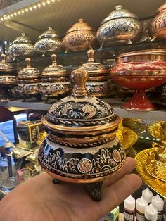 a hand holding an ornately decorated container in front of many other decorative items on display