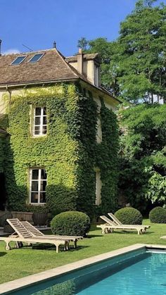 an outdoor swimming pool surrounded by lush green plants and lawn furniture next to a large house