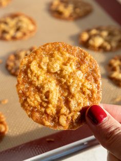 a person holding up a cookie in front of a baking pan filled with cookies on it