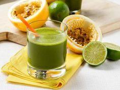 a green smoothie in a glass next to sliced limes and oranges on a cutting board