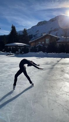 a person skating on an ice rink in front of a house with mountains in the background