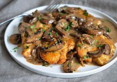 a white plate topped with chicken covered in mushroom gravy next to a fork