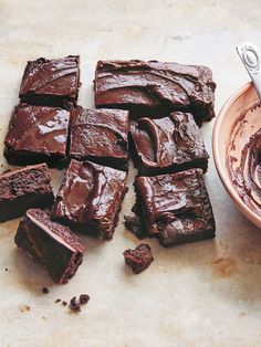 chocolate brownies cut into squares next to a bowl of frosting on a table