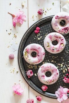 four donuts with pink frosting and sprinkles on a metal tray