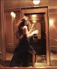 a woman in a long dress is walking through an open door with her hair blowing in the wind