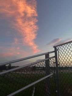 the sky is pink and blue as it sits behind a chain link fence at sunset