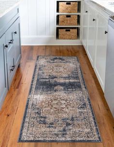 a large rug in the middle of a kitchen with white cabinets and wooden flooring