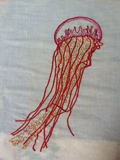 an embroidered jellyfish is shown on a piece of linen with red thread and beads