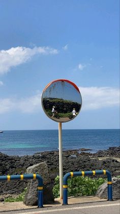 there is a mirror on the side of the road by the ocean and people in it