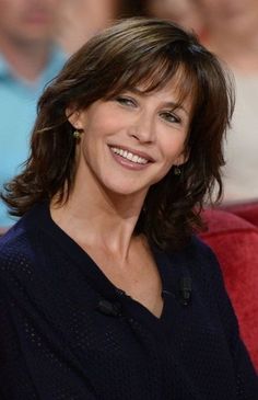 a smiling woman sitting on top of a red couch in front of a group of people