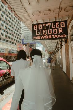 two people walking down the sidewalk in front of a building with a sign that says bottled liquor newsstand