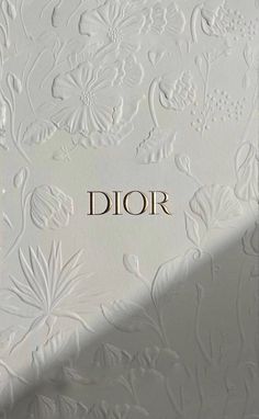 the word dior is written in gold on a white wall with floral designs and leaves