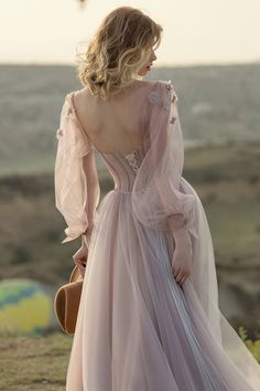 a woman in a pink dress standing on top of a hill with her back to the camera