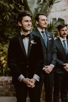 three men in tuxedos standing next to each other with one holding his hand