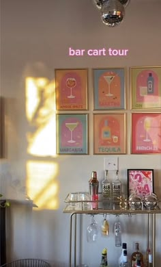 a bar cart with wine glasses and bottles on it in front of several framed pictures