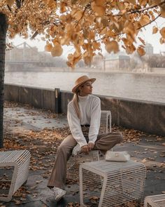 a woman sitting on top of a white bench next to a tree with leaves all over it