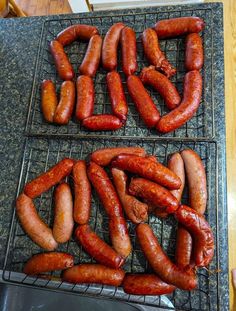 two trays filled with cooked hot dogs on top of a grill next to a sink