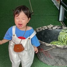 a young child standing next to a basket full of watermelon