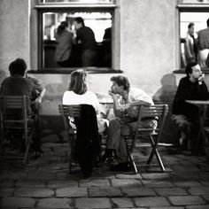 black and white photograph of people sitting at tables in front of a building with open windows